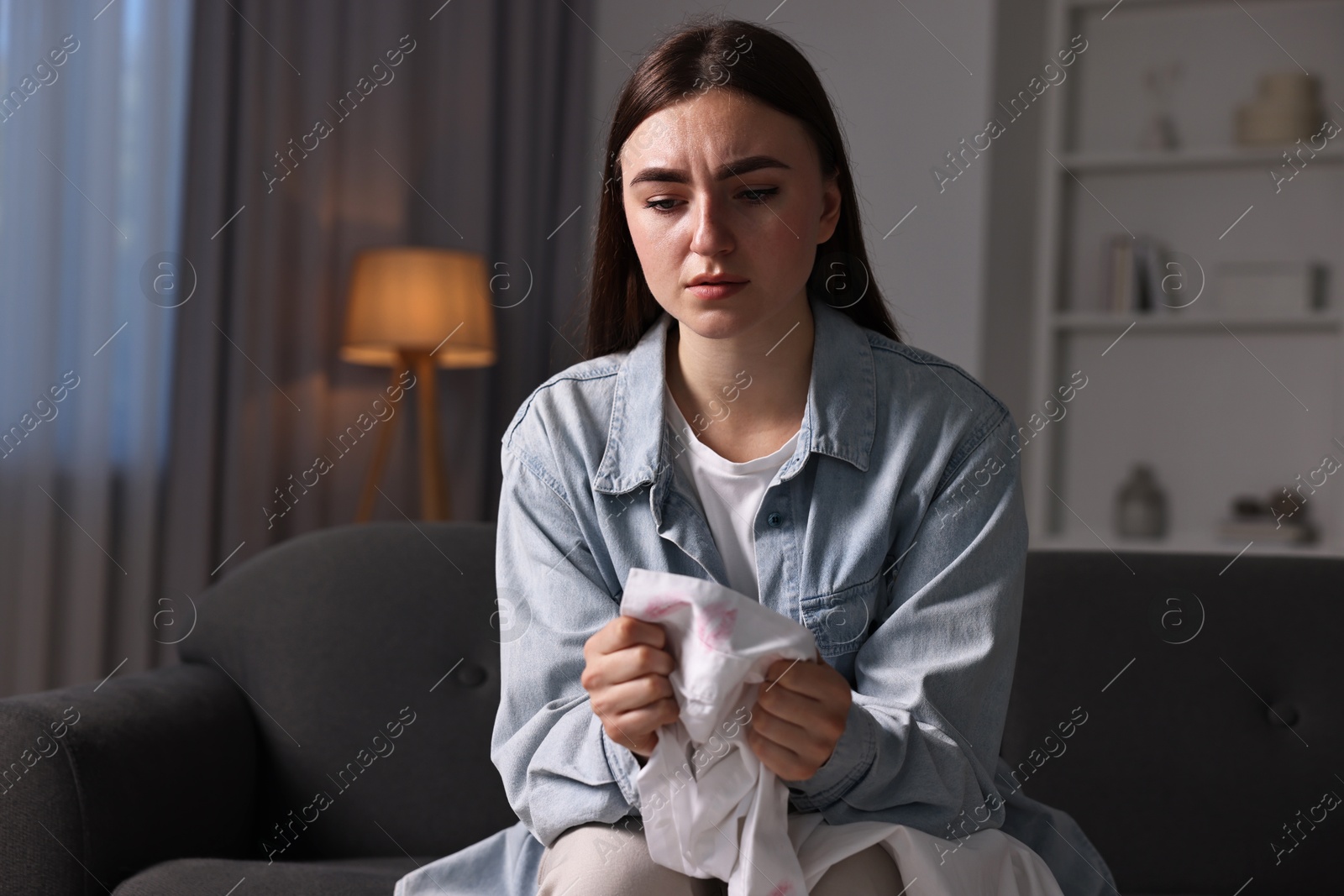 Photo of Frustrated wife holding shirt with lipstick marks as proof of her unfaithful husband at home