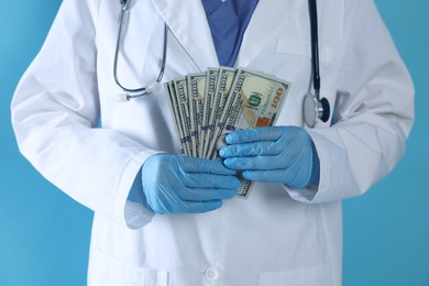 Photo of Corruption concept. Doctor with dollar banknotes on light blue background, closeup