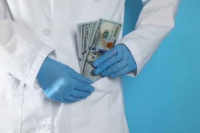 Photo of Corruption concept. Doctor putting dollar banknotes into her pocket on light blue background, closeup