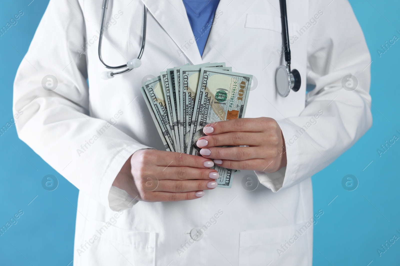 Photo of Corruption concept. Doctor with dollar banknotes on light blue background, closeup