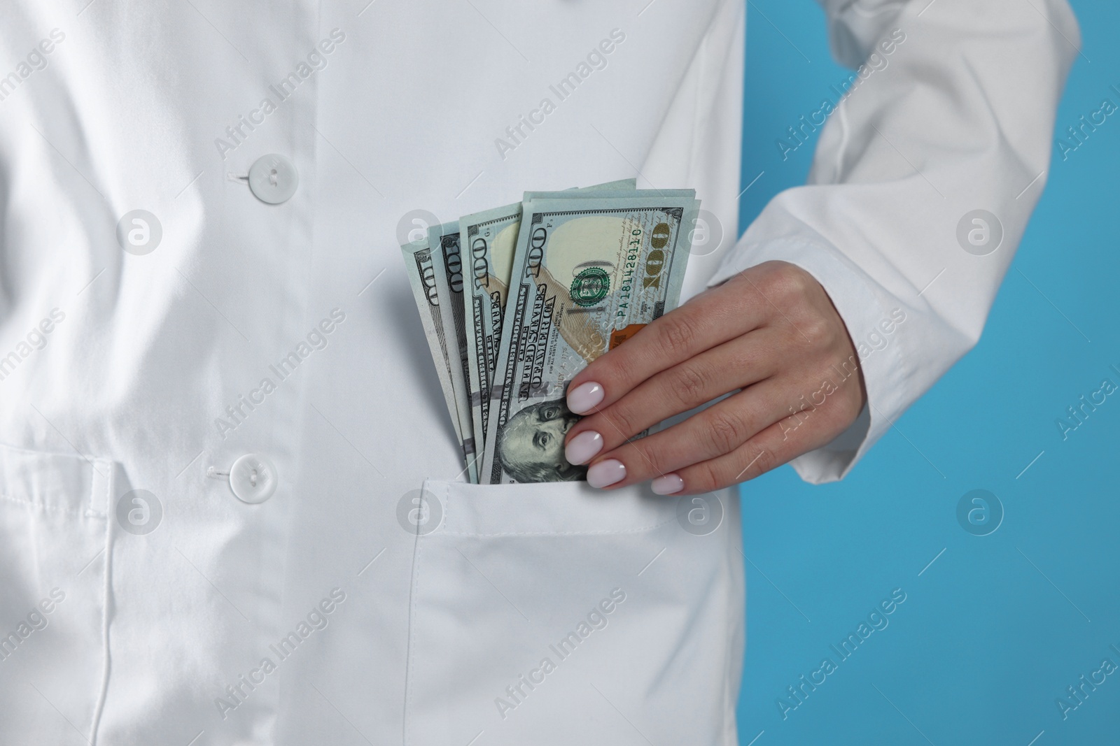 Photo of Corruption concept. Doctor putting dollar banknotes into her pocket on light blue background, closeup