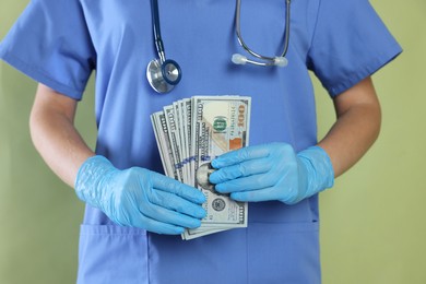 Photo of Corruption concept. Doctor with dollar banknotes on green background, closeup