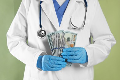 Photo of Corruption concept. Doctor with dollar banknotes on green background, closeup