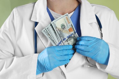 Photo of Corruption concept. Doctor putting dollar banknotes into her coat on green background, closeup