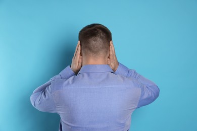 Photo of Man covering his ears on light blue background, back view