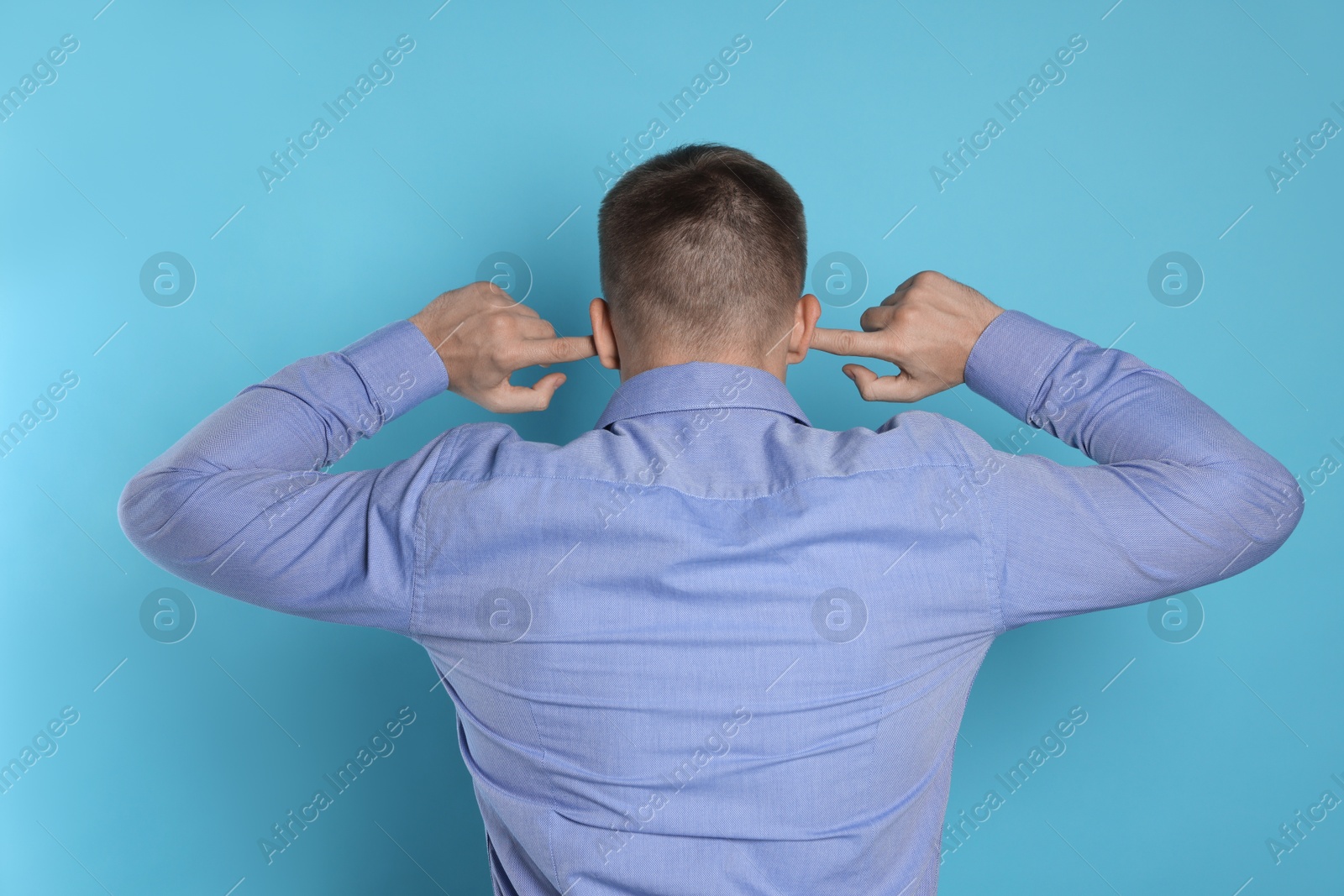 Photo of Man covering his ears with fingers on light blue background, back view