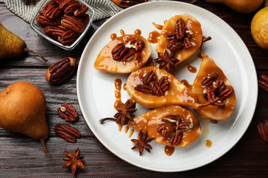 Photo of Delicious pears with caramel sauce, pecan nuts and spices on wooden table, flat lay