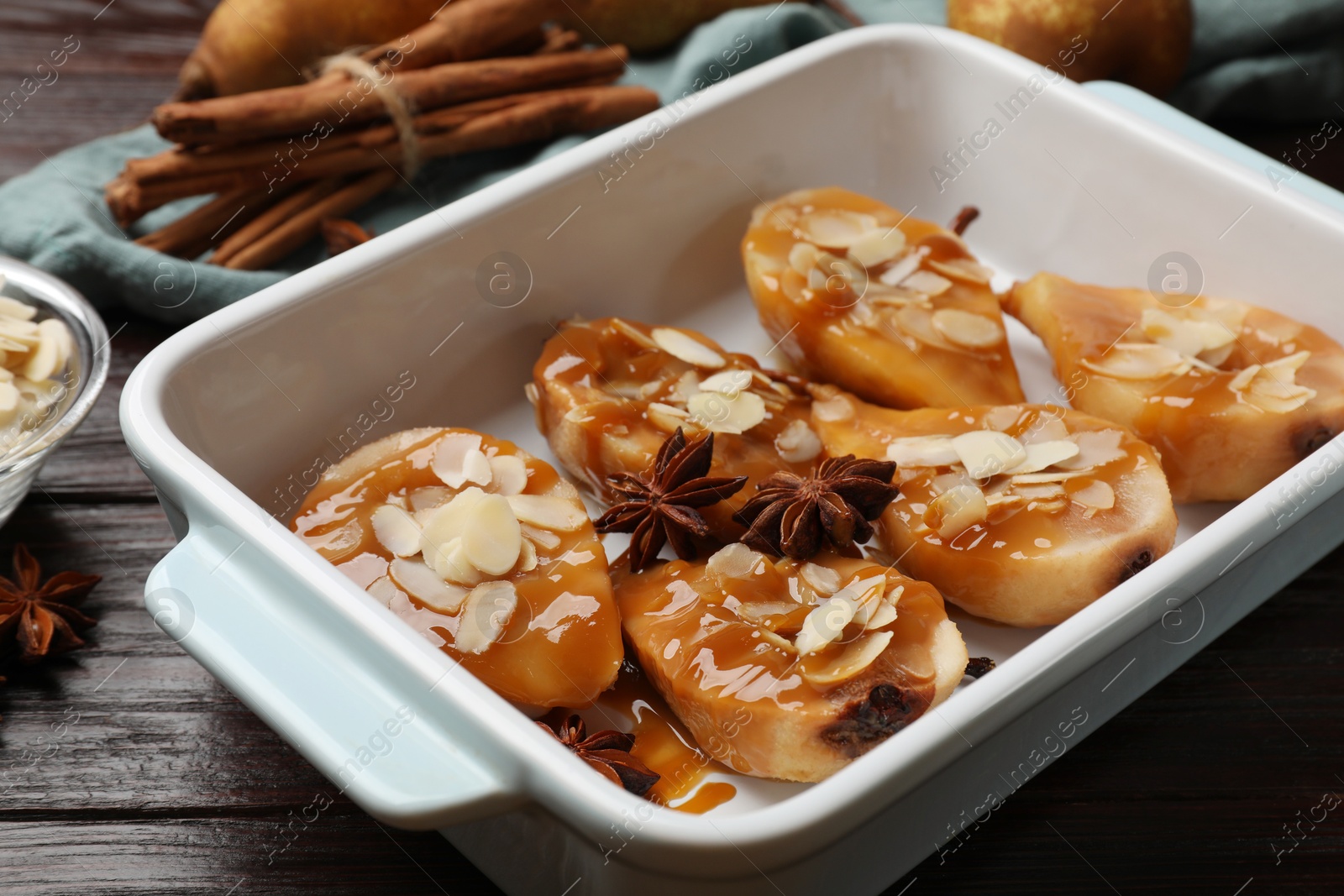 Photo of Delicious pears with caramel sauce, almond flakes and anise stars on wooden table, closeup