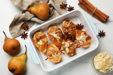 Photo of Delicious pears with caramel sauce, almond flakes and spices on white marble table, flat lay