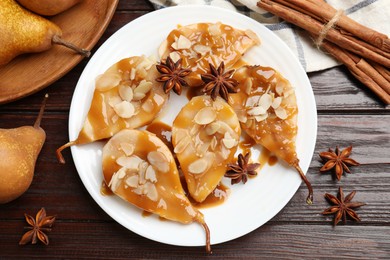 Photo of Delicious pears with caramel sauce, almond flakes and spices on wooden table, top view