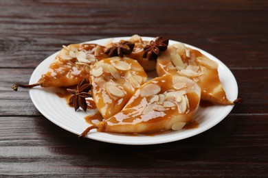 Photo of Delicious pears with caramel sauce, almond flakes and anise stars on wooden table, closeup