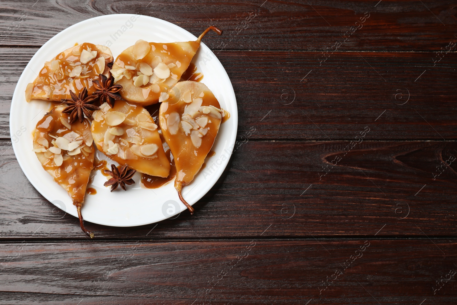 Photo of Delicious pears with caramel sauce, almond flakes and anise stars on wooden table, top view. Space for text