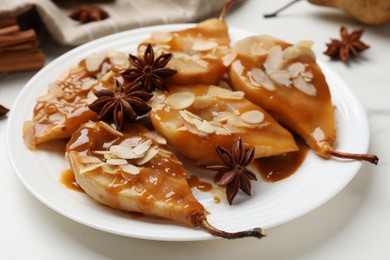 Photo of Delicious pears with caramel sauce, almond flakes and anise stars on white table, closeup