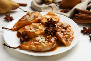 Photo of Delicious pears with caramel sauce, almond flakes and anise stars on white table, closeup