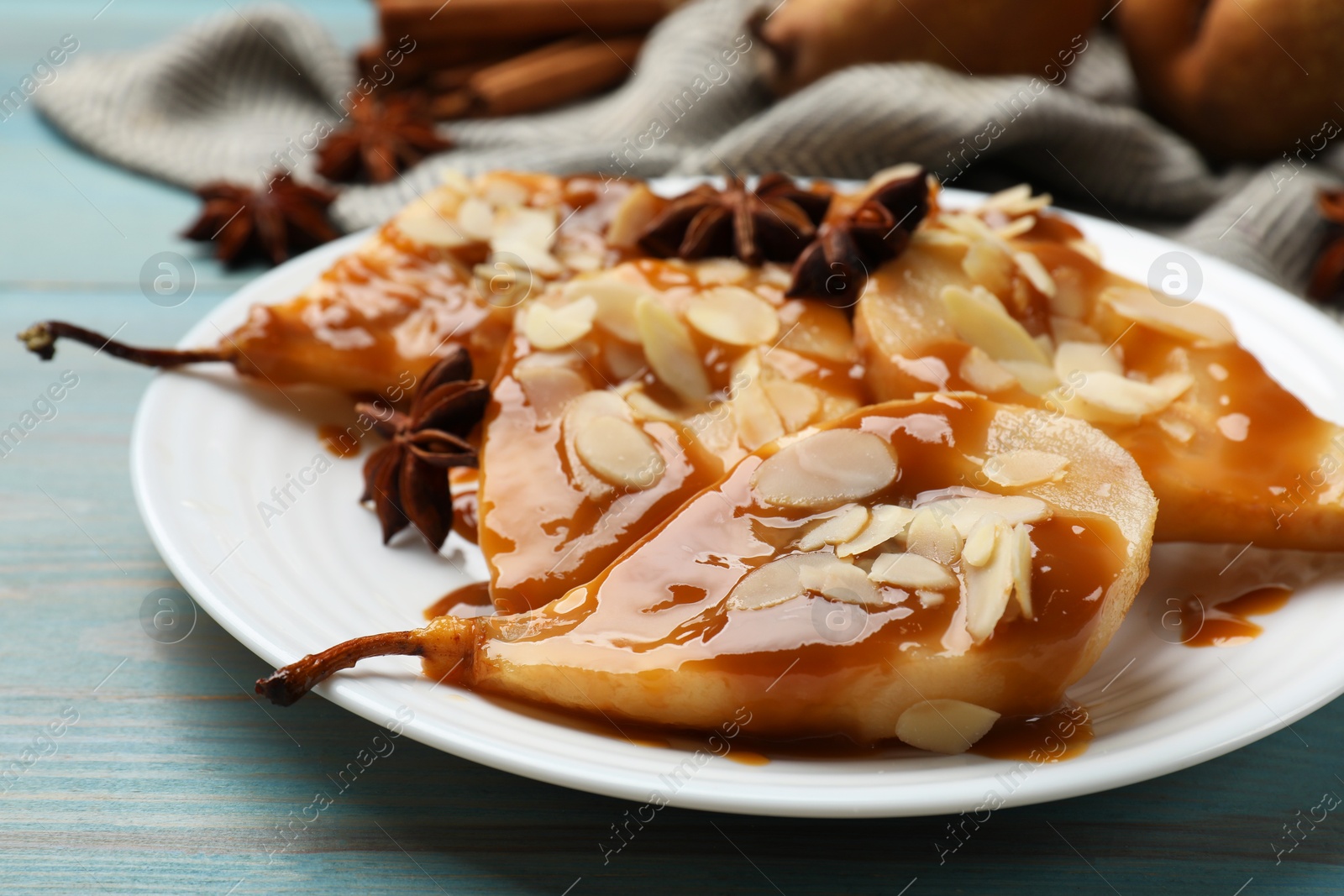 Photo of Delicious pears with caramel sauce, almond flakes and anise stars on light blue wooden table, closeup