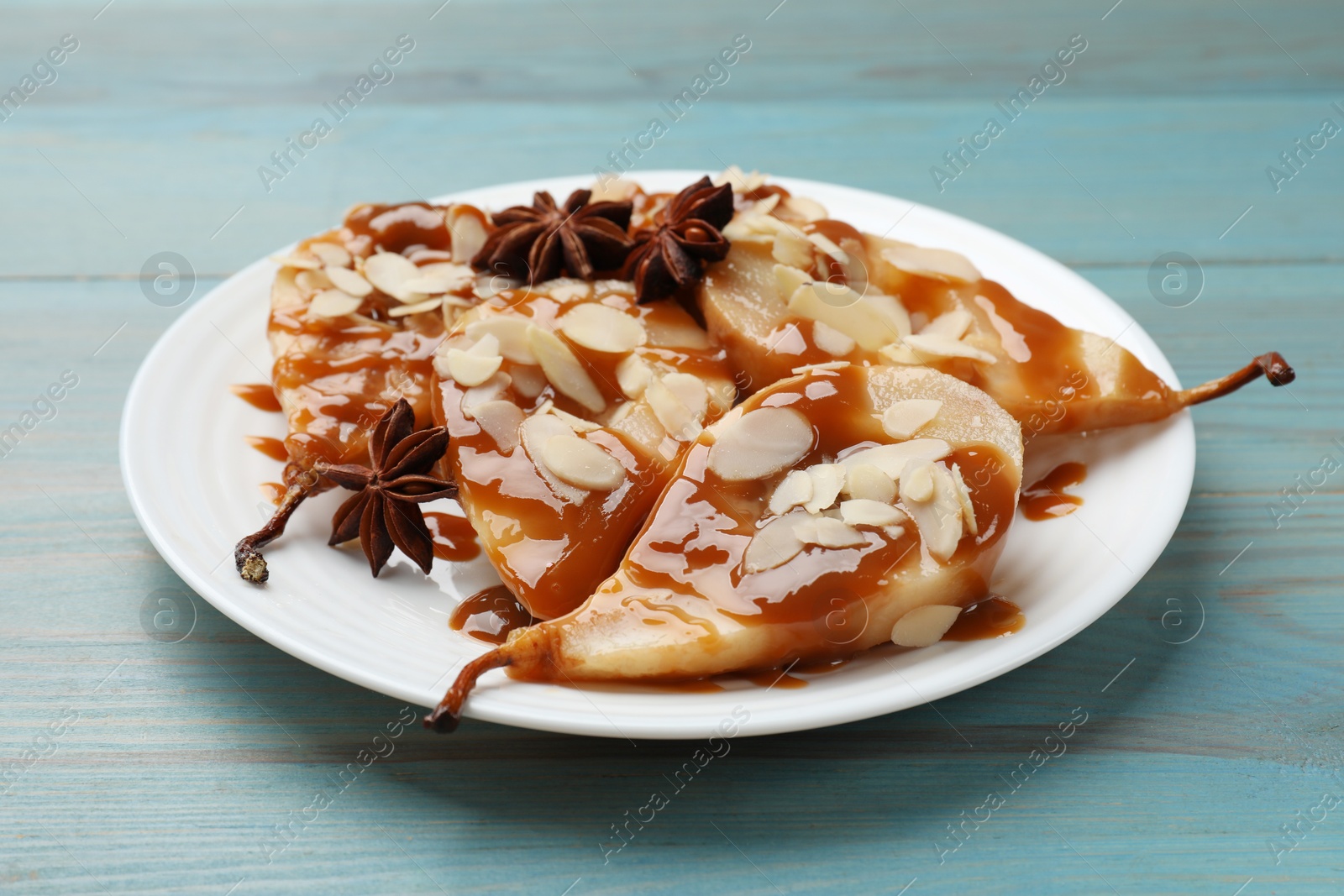 Photo of Delicious pears with caramel sauce, almond flakes and anise stars on light blue wooden table, closeup