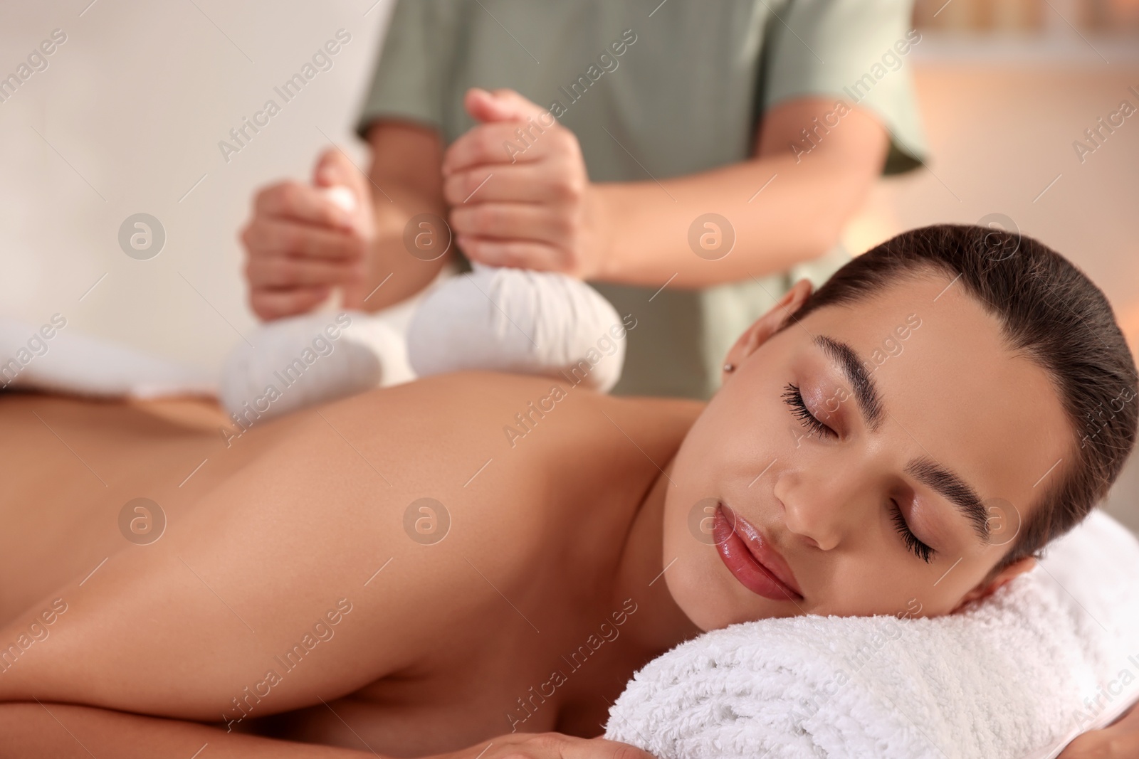 Photo of Woman receiving back massage with herbal bags in spa salon