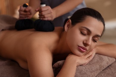 Photo of Woman receiving back massage with herbal bags in spa salon