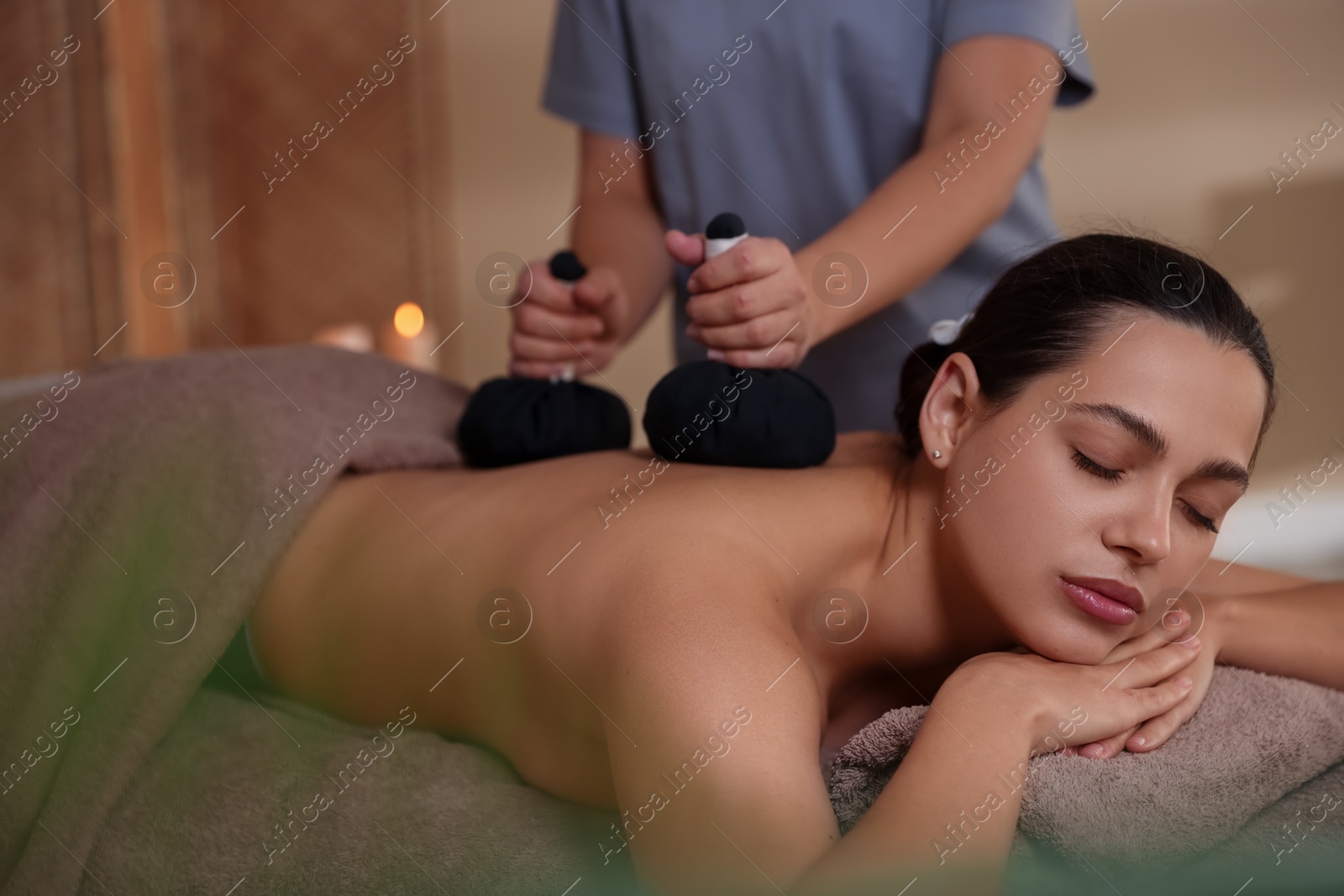 Photo of Woman receiving back massage with herbal bags in spa salon