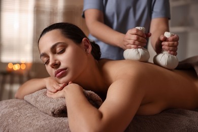 Photo of Woman receiving back massage with herbal bags in spa salon