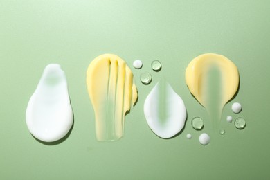 Photo of Cream and gel samples on light green background, flat lay