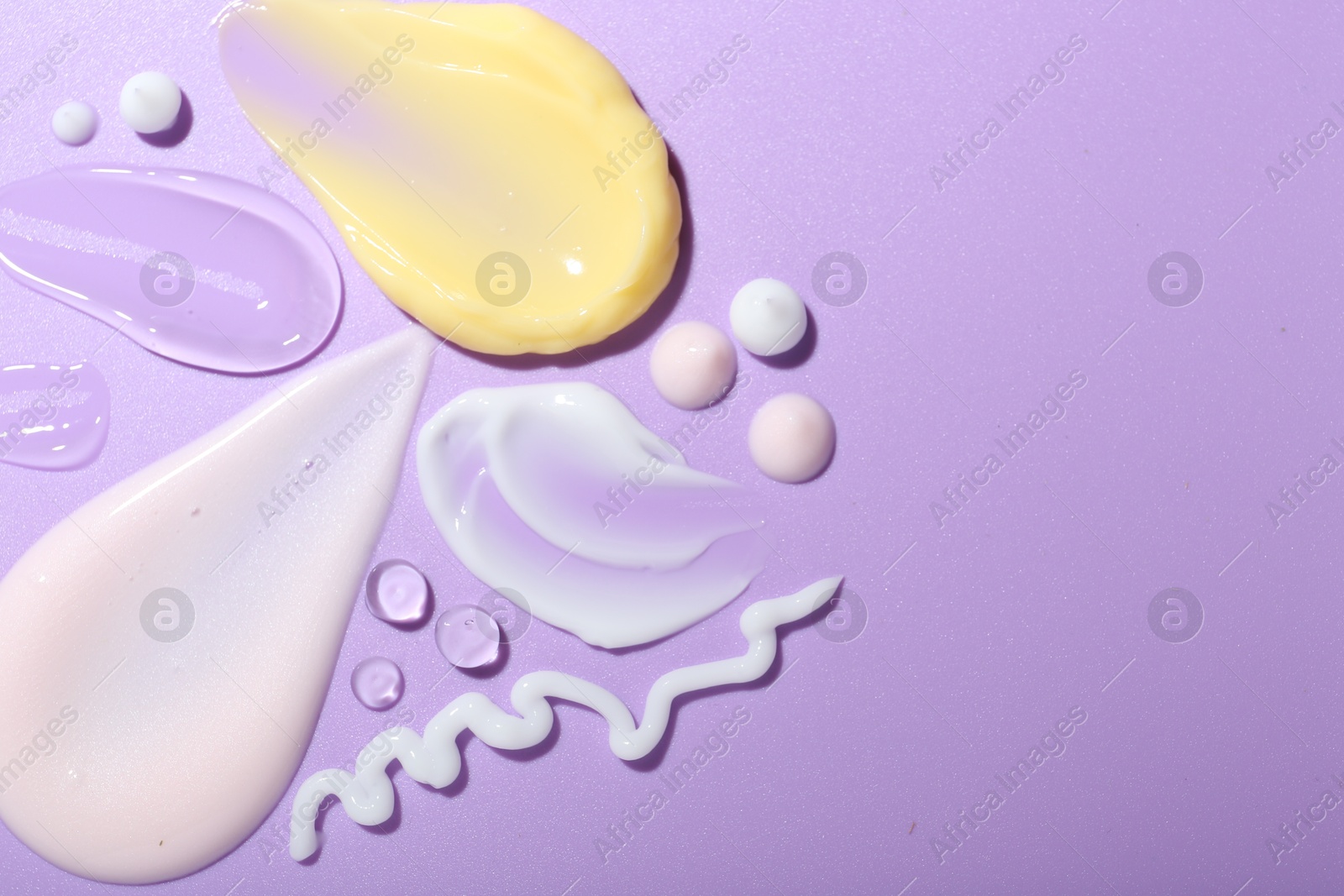 Photo of Cream and gel samples on violet background, top view. Space for text