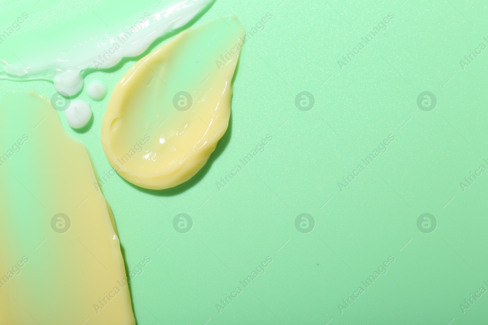 Photo of Cream samples on light green background, top view. Space for text