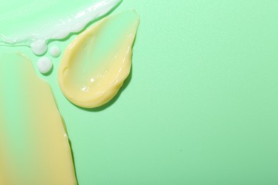 Photo of Cream samples on light green background, top view. Space for text