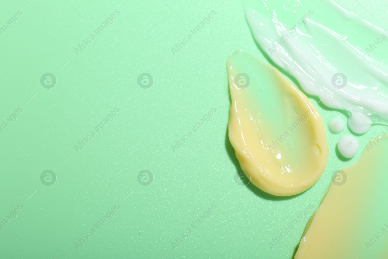 Photo of Cream samples on light green background, top view. Space for text