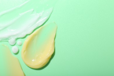 Photo of Cream samples on light green background, top view. Space for text