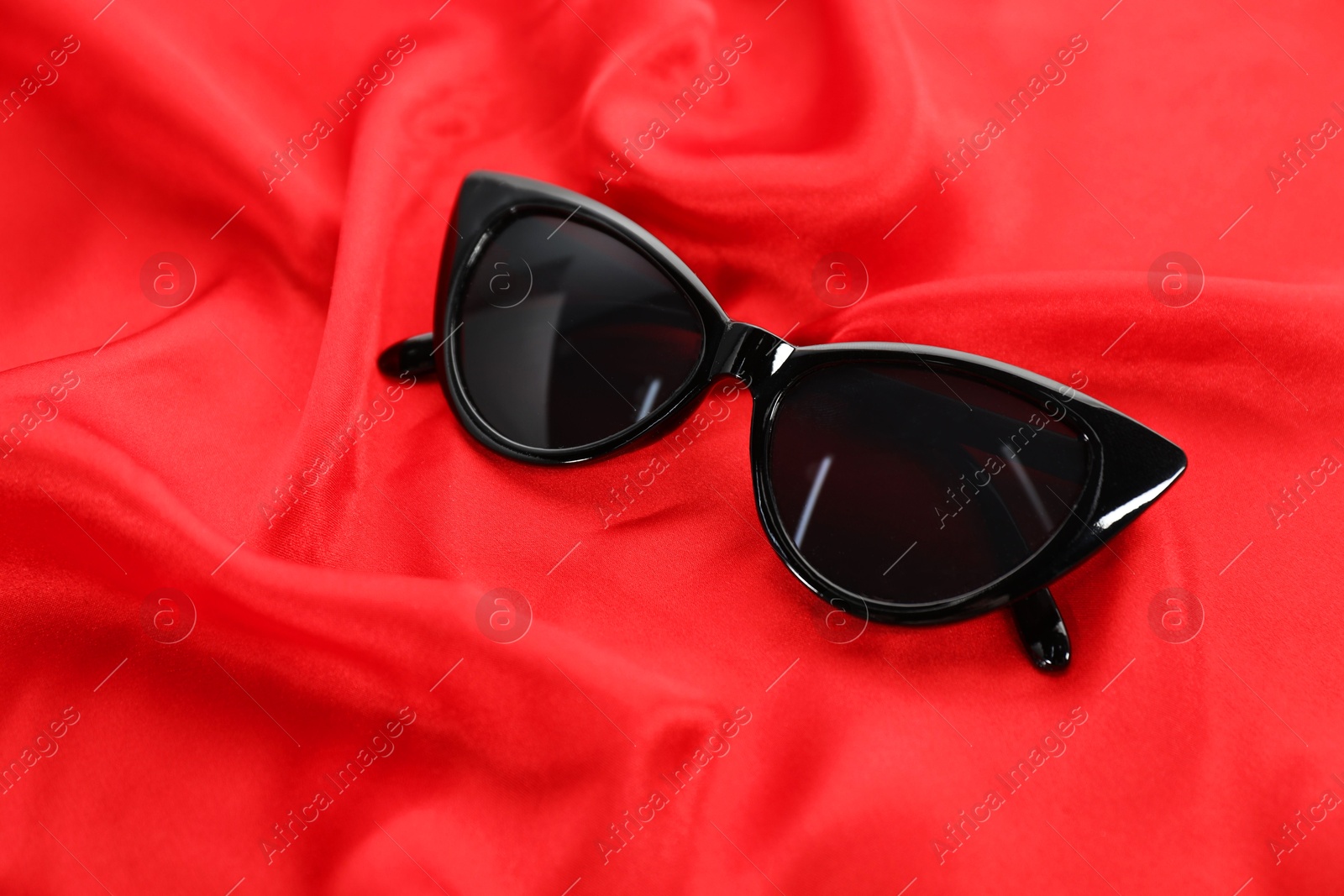 Photo of Stylish sunglasses on red fabric. Elegant accessory