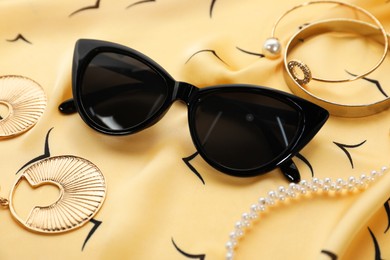 Photo of Stylish sunglasses and jewelry on beige fabric