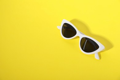 Photo of Stylish sunglasses on yellow background, top view. Space for text