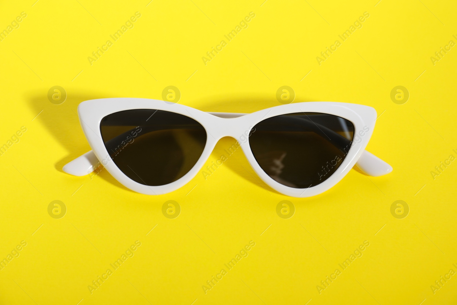 Photo of Stylish sunglasses on yellow background. Elegant accessory