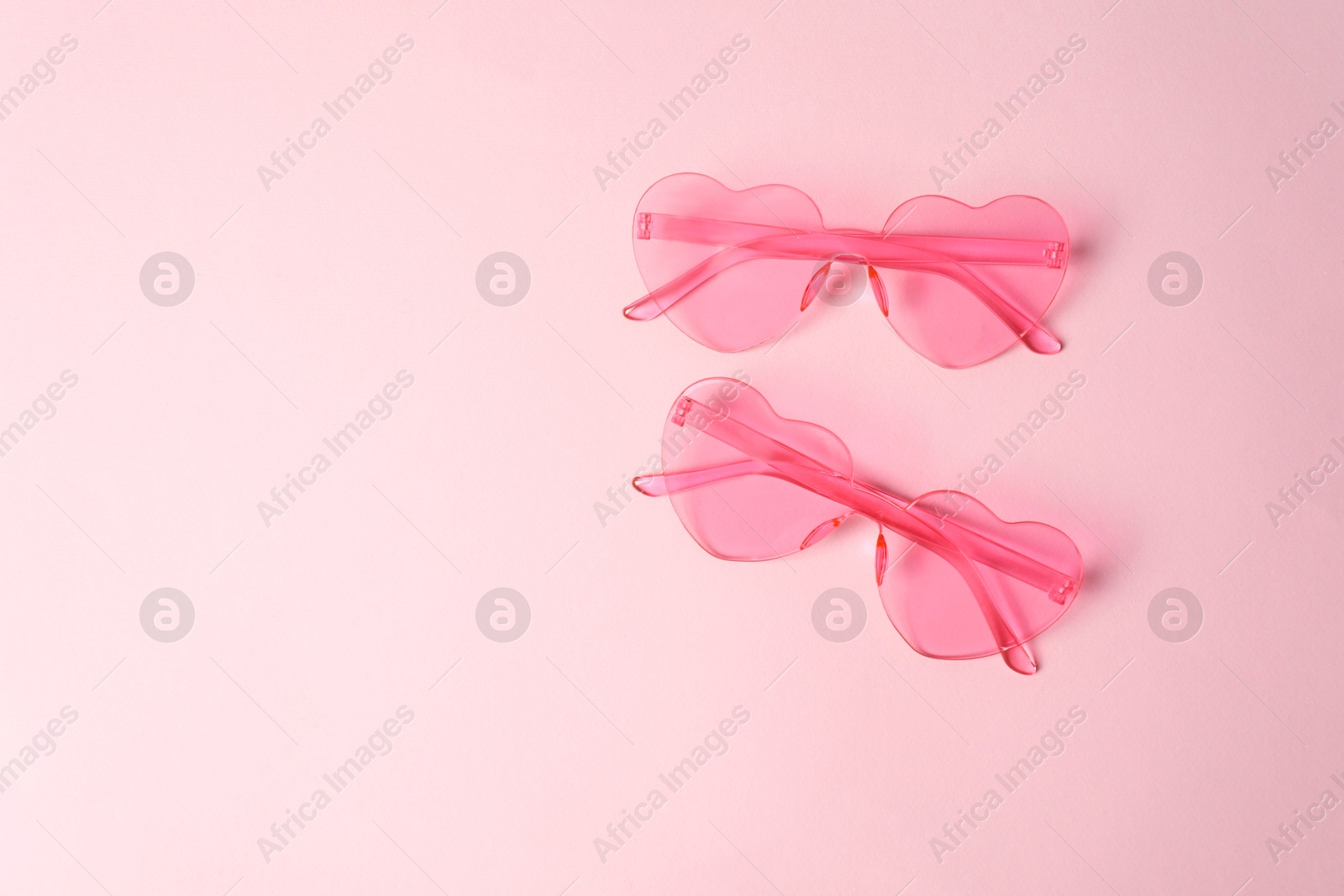 Photo of Stylish heart shaped sunglasses on pink background, top view. Space for text