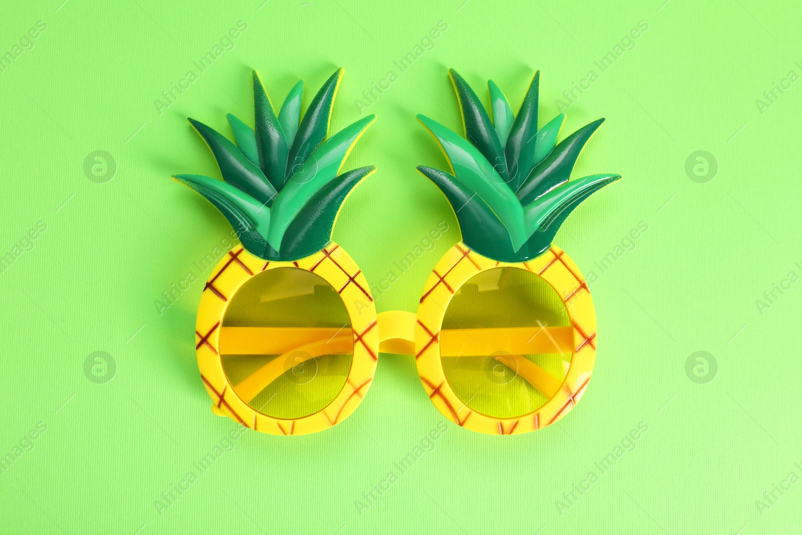 Photo of Creative pineapple shaped sunglasses on green background, top view