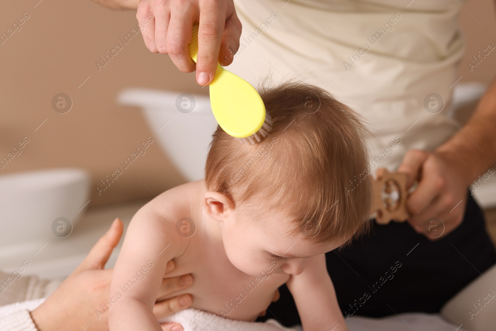 Photo of Parents brushing hair of their little baby indoors, closeup