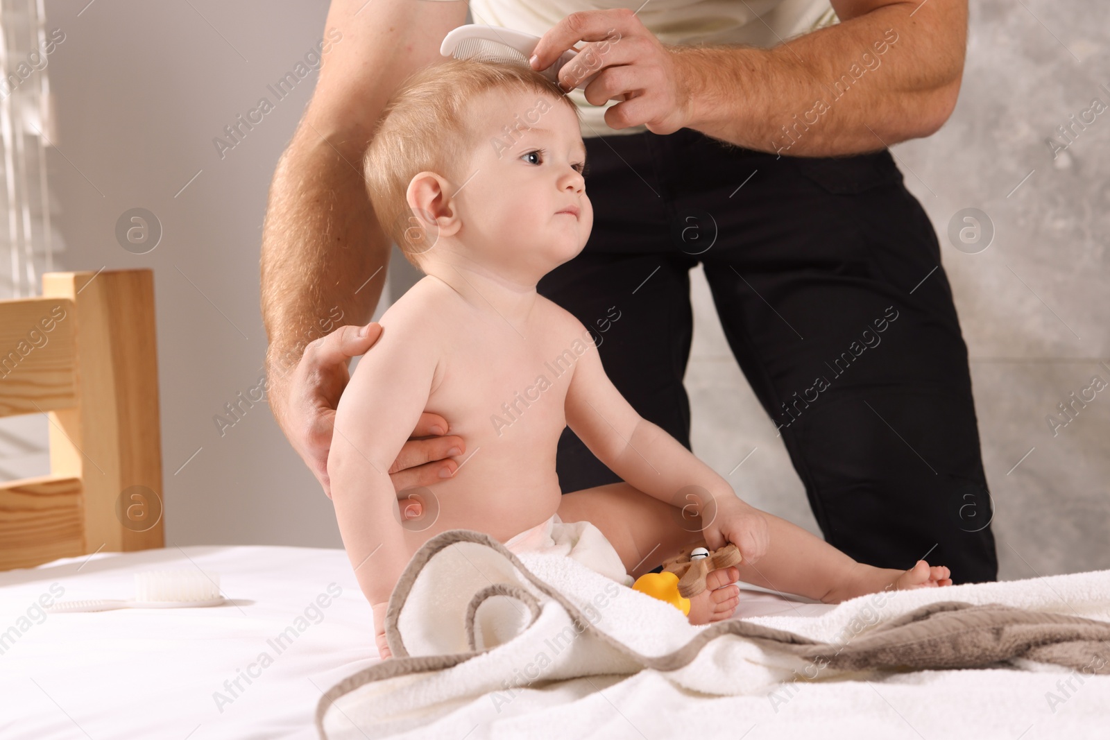 Photo of Man combing hair of his little baby indoors, closeup