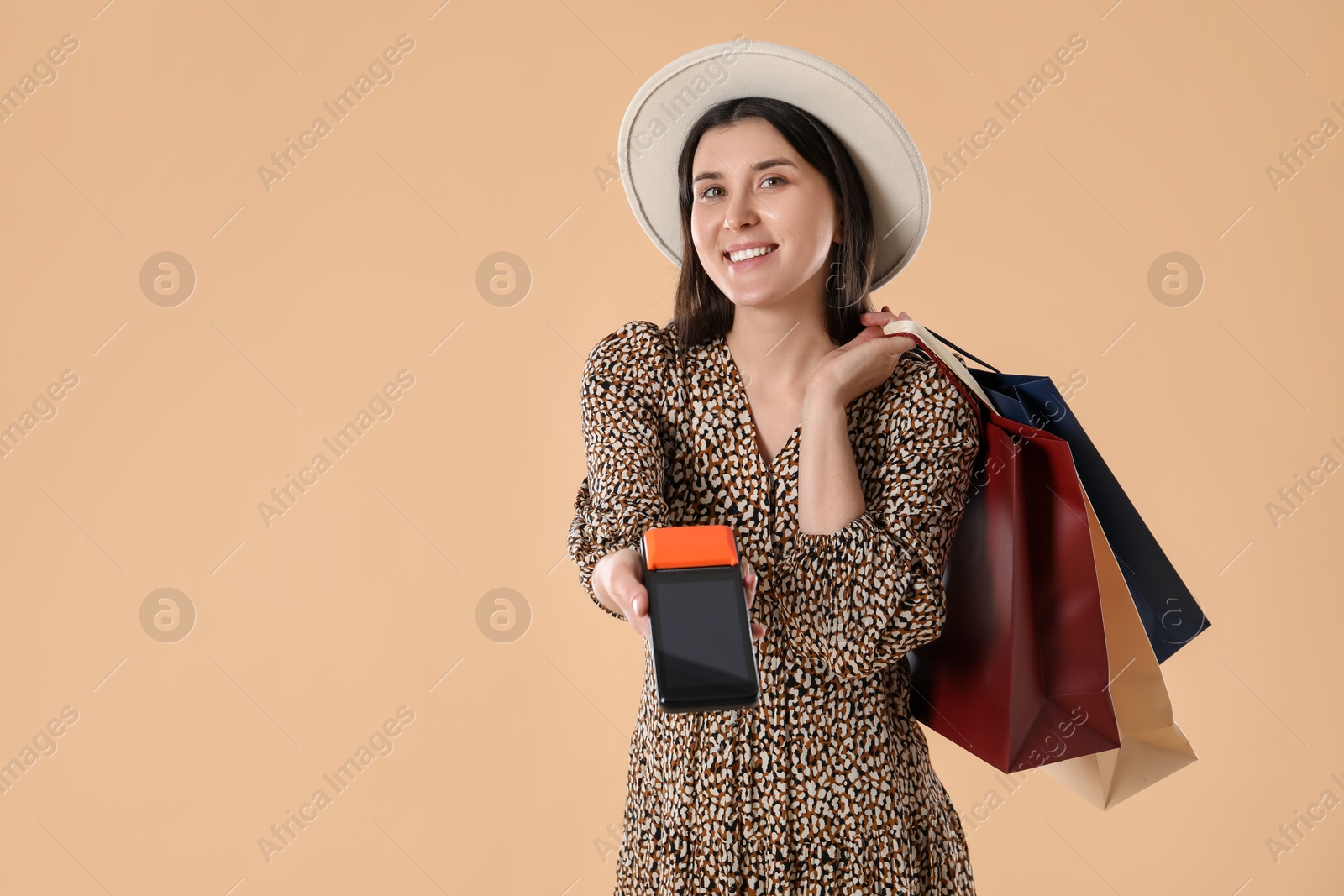 Photo of Happy young woman with payment terminal and shopping bags on beige background, space for text