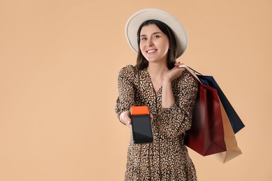 Happy young woman with payment terminal and shopping bags on beige background, space for text