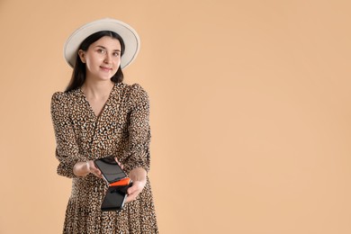 Young woman with payment terminal and smartphone on beige background, space for text