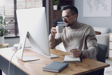 Photo of Handsome man working with computer at desk indoors. Home office