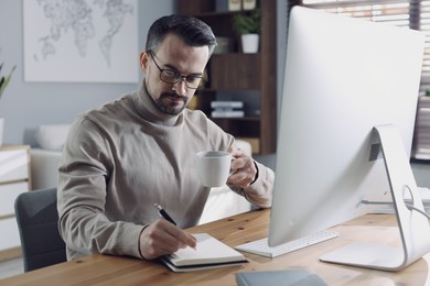 Handsome man working with computer at desk indoors. Home office