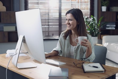 Happy woman working with computer at desk indoors. Home office