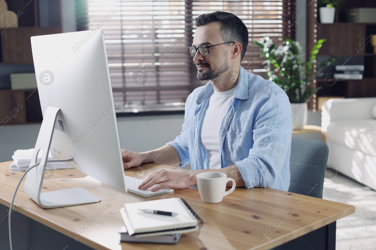 Photo of Handsome man working with computer at desk indoors. Home office