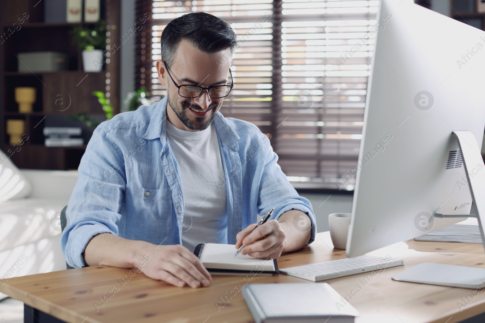 Photo of Happy man working with computer at desk indoors. Home office