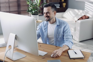 Happy man working with computer at desk indoors. Home office