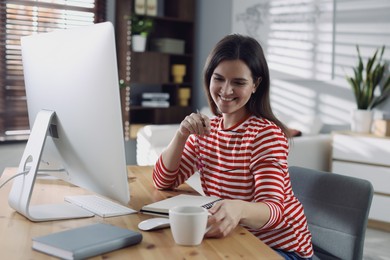 Photo of Happy woman working with computer at desk indoors. Home office