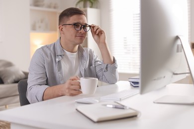 Handsome man working with computer at desk indoors. Home office