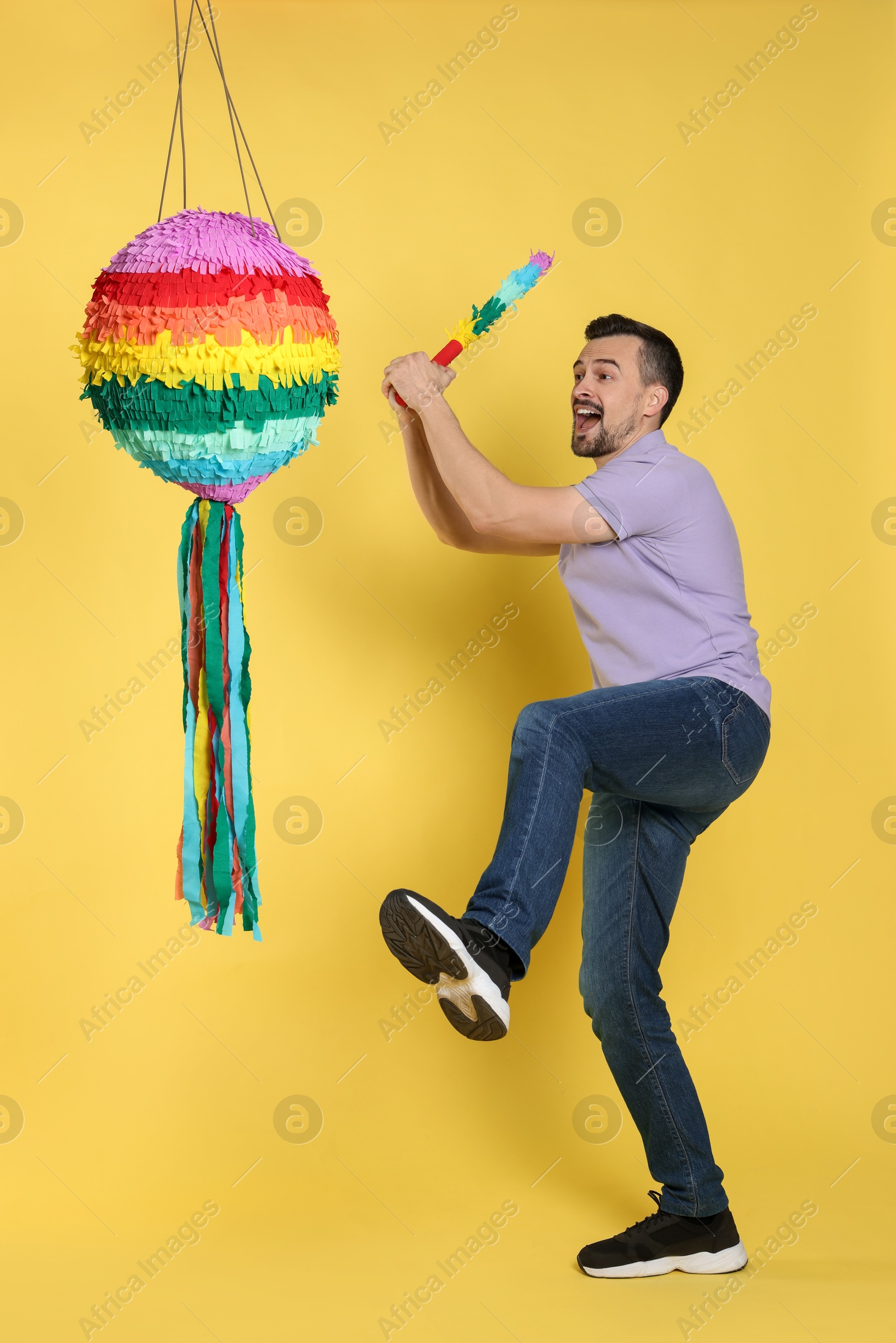 Photo of Emotional man hitting colorful pinata with stick on yellow background